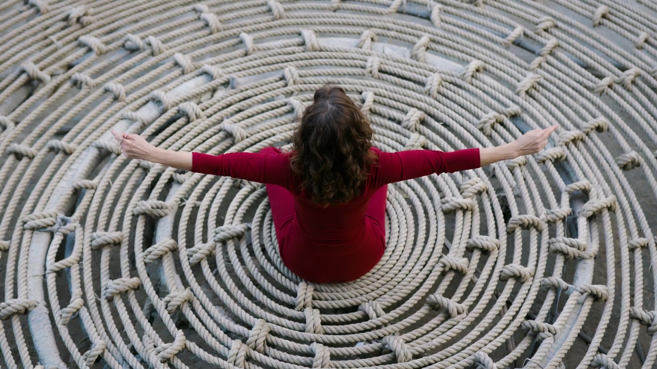 Donna seduta di spalle e con le braccia aperte su un pavimento di corde che formano una composizione circolare